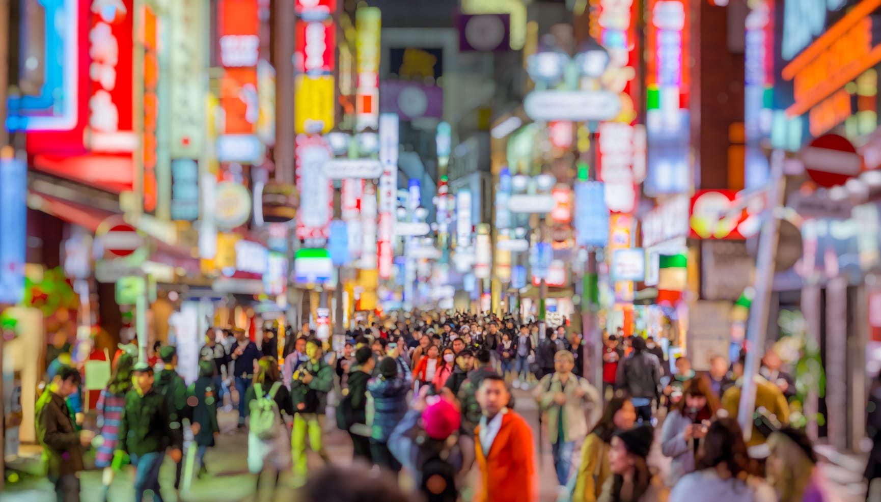 Blurred image of a busy crowded Tokyo street lit up with neon signs.